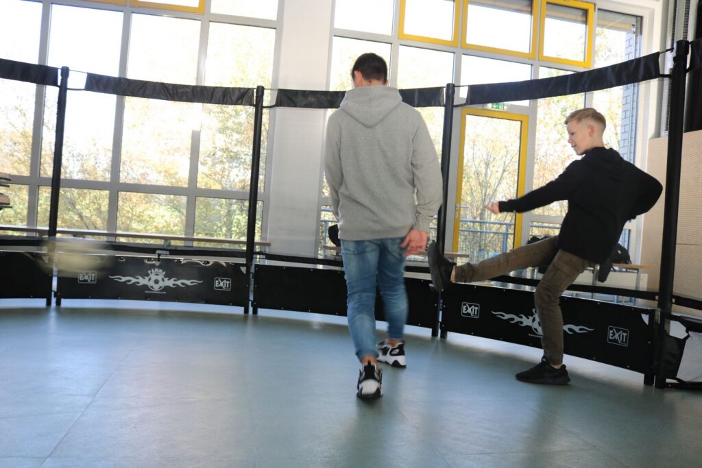 Zwei Schüler spielen Fußball in einem Raum mit Netzen.