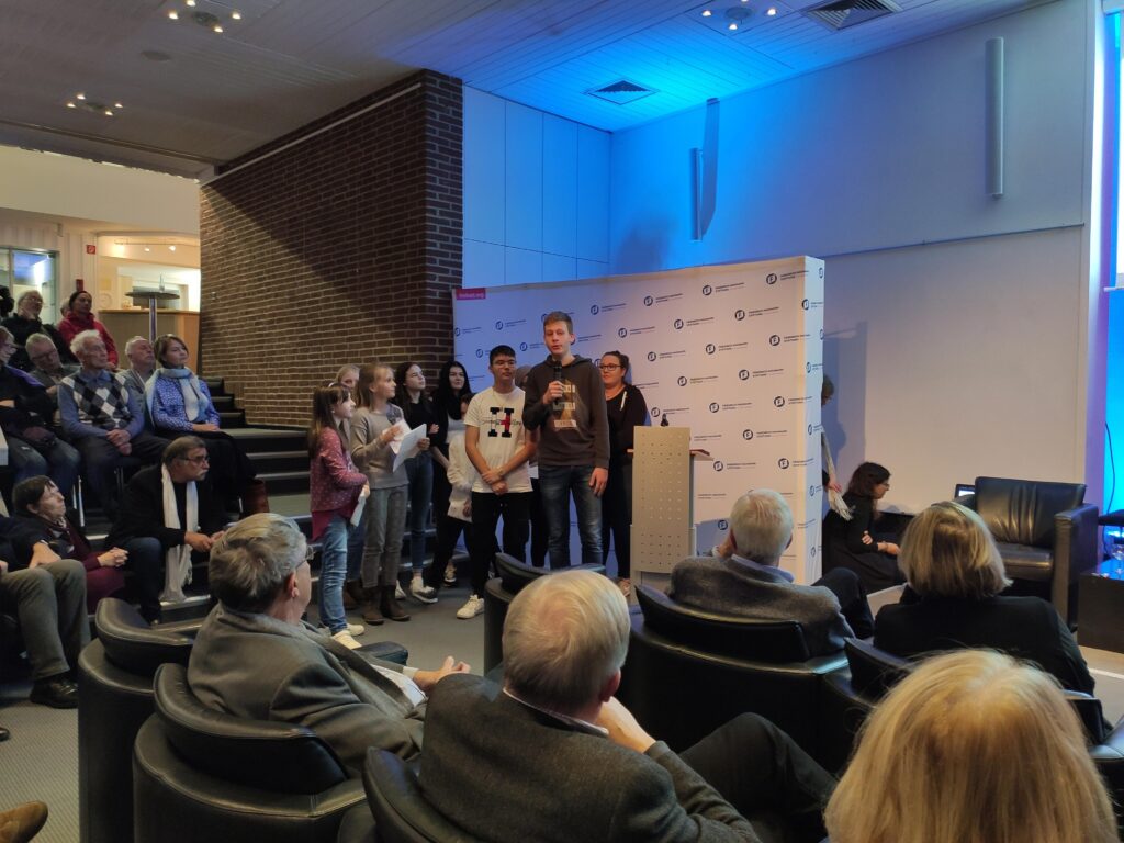 Schüler stehen auf der Bühne bei einer Veranstaltung vor Publikum.