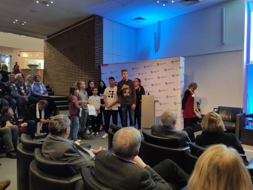 Gruppe von Schülern steht auf einer Bühne während einer Veranstaltung in einem Saal.