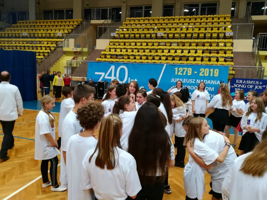 Schülerinnen und Schüler in weißen T-Shirts versammeln sich in einer Sporthalle.