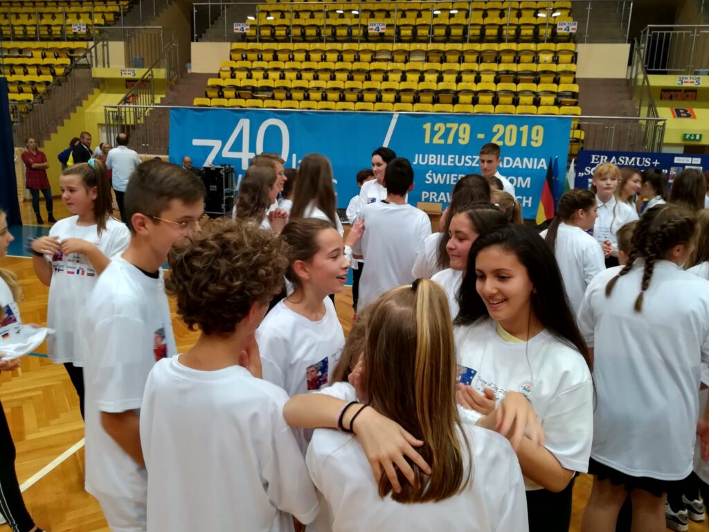 Gruppierung von Schülern in weißen T-Shirts in einer Sporthalle.