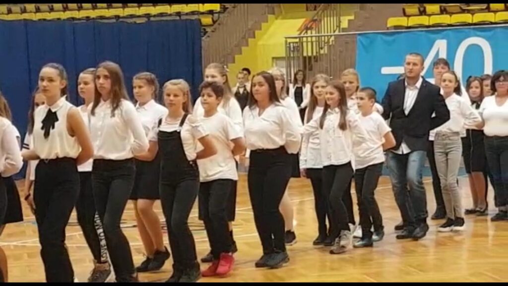 Schülerinnen und Schüler in einheitlicher Kleidung bei einer Aufführung in einer Turnhalle.