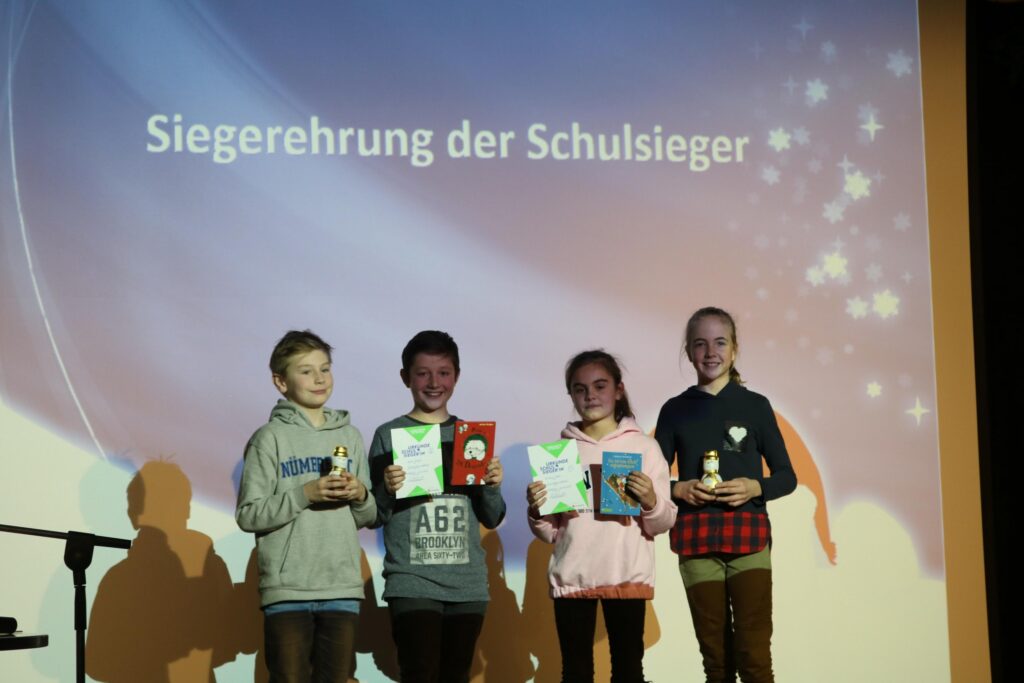 Siegerverleihung mit vier Kindern, die Pokale und Urkunden halten.