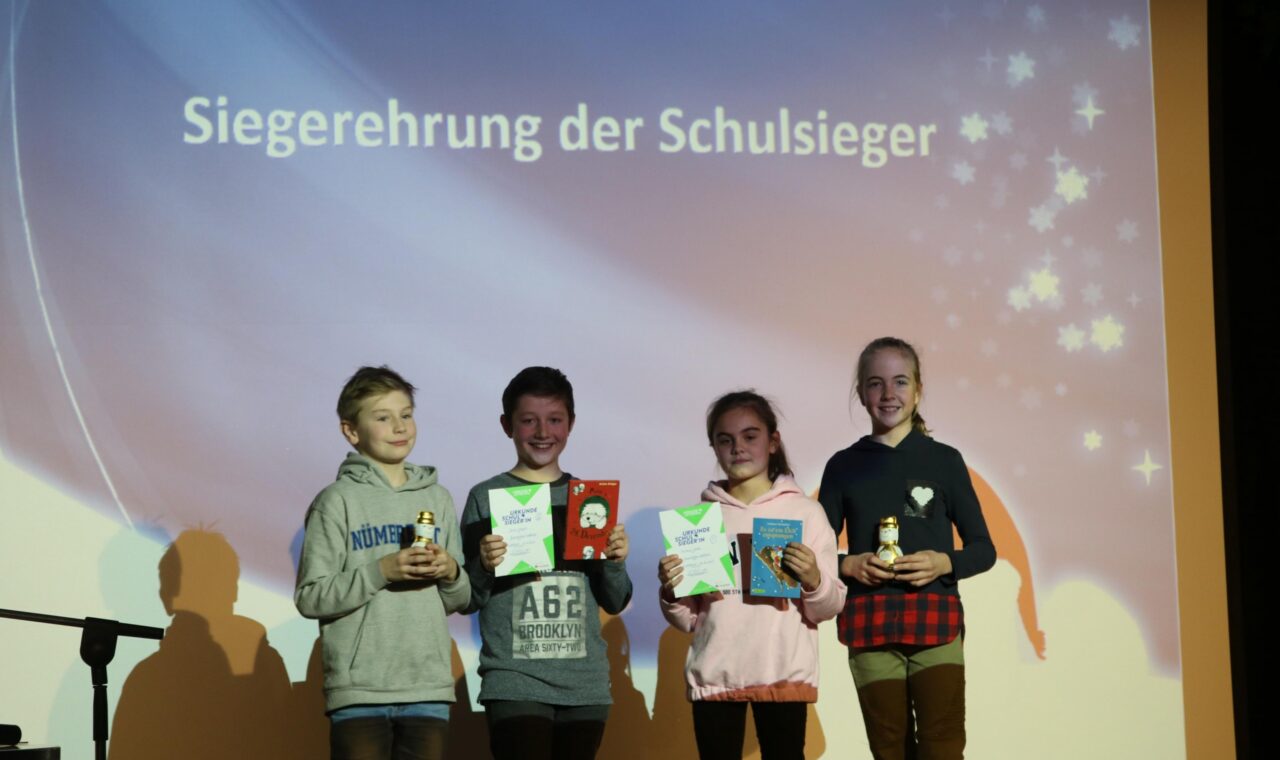 Siegerverleihung mit vier Kindern, die Pokale und Urkunden halten.