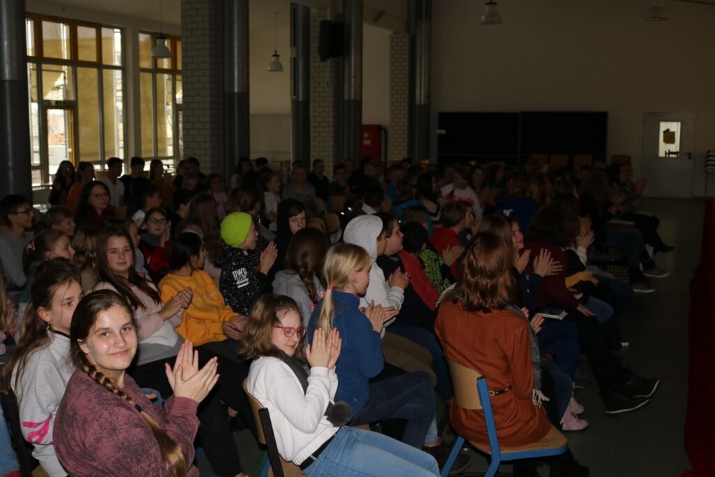 Schüler sitzen in einem Saal und applaudieren.