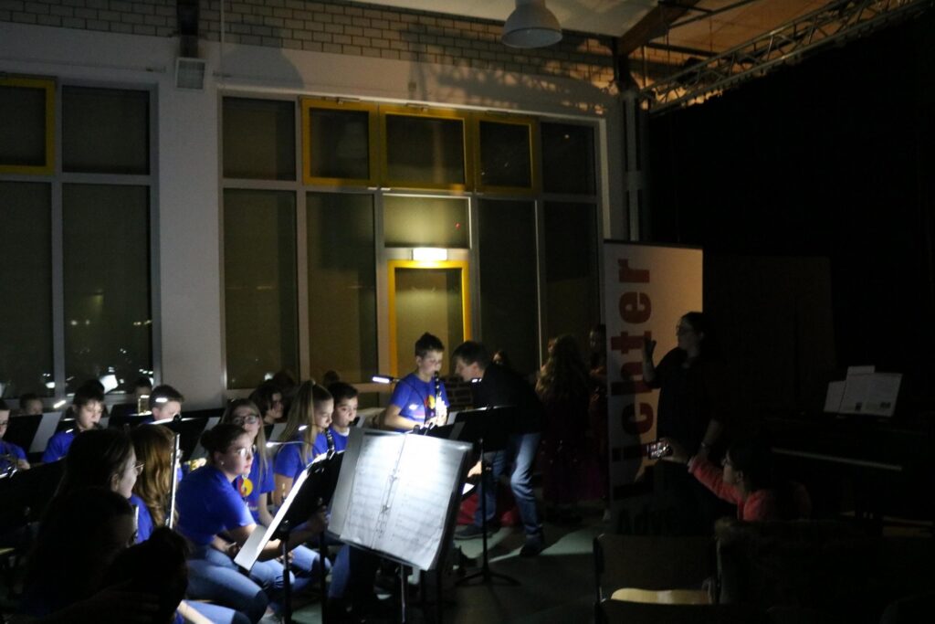 Schüler spielen im Dunkeln in einem Musikraum. Einige sind mit Notenblättern beschäftigt.