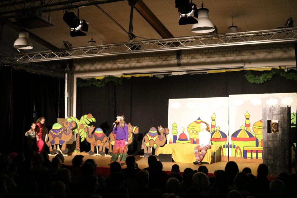 Aufführung mit bunten Kulissen, Kamelen und Schauspielern auf der Bühne.