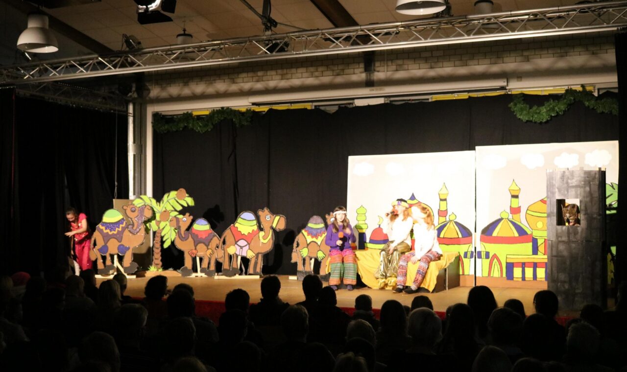Bühne mit Kamelen und Darstellern in bunten Kostümen während einer Theateraufführung.