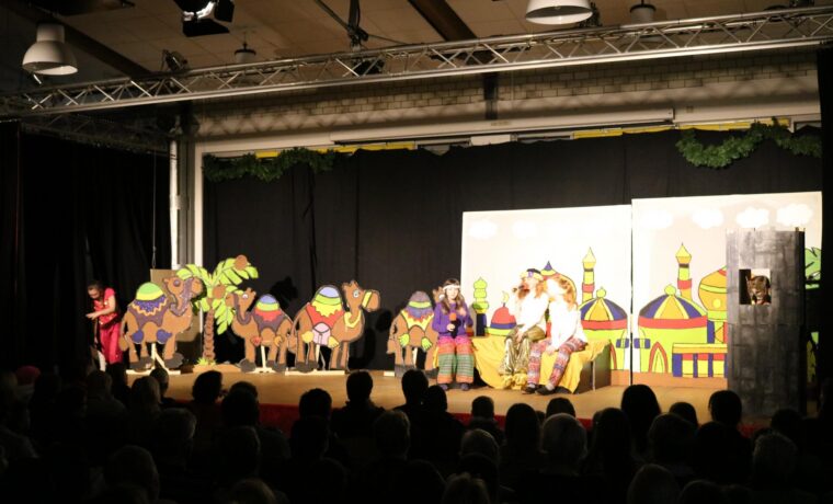 Bühne mit Kamelen und Darstellern in bunten Kostümen während einer Theateraufführung.
