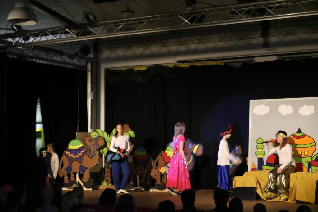 Theateraufführung mit Schülern in historischen Kostümen auf einer Bühne.