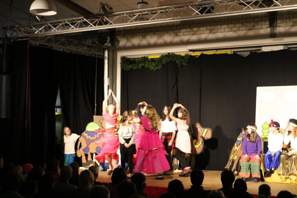 Schülerschauspiel auf der Bühne mit verkleideten Kindern und Kulissen.