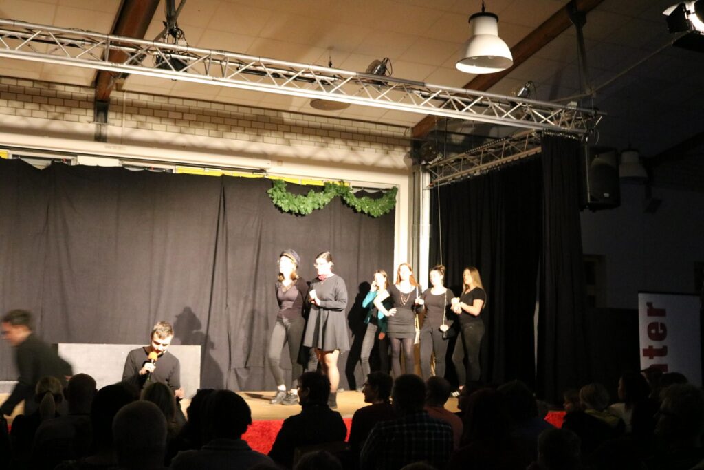 Theateraufführung mit mehreren Darstellerinnen auf der Bühne vor einem Publikum.