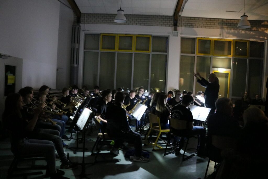 Musikgruppe in einem dunklen Raum mit einem Dirigenten und Notenständern.