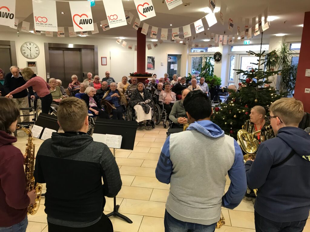 Musiker spielen für Bewohner in festlich geschmücktem Raum mit Tannenbaum.