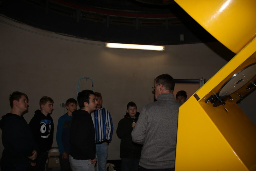 Gruppe von Schülern in einer Sternwarte, die einem Vortrag lauschen.