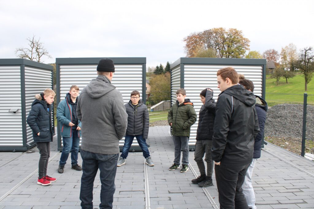 Gruppe von Schülern steht in einem Kreis auf einem Platz im Freien.