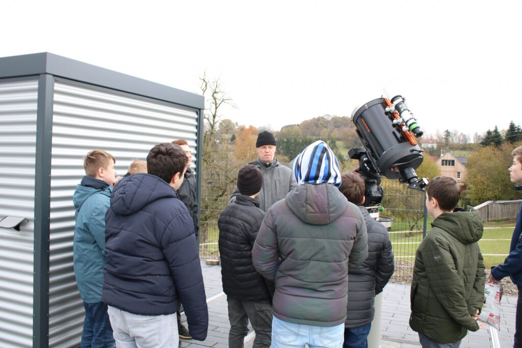 Gruppe von Schülern beobachtet mit Fernrohr auf einem Dach.