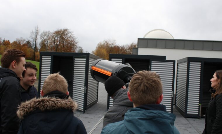 Gruppe von jungen Menschen betrachtet ein Teleskop vor einem Observatorium.