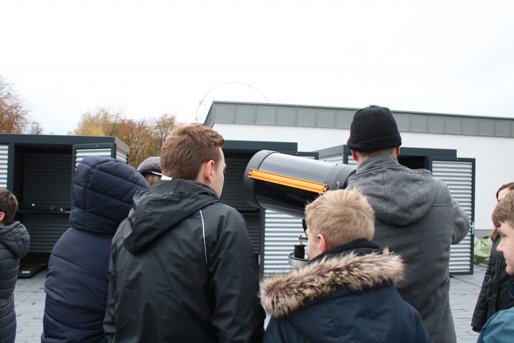 Schüler schauen gemeinsam durch ein Teleskop auf dem Schulgelände.