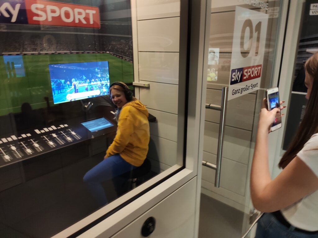 Person sitzt in einem Monitorraum bei Sky Sport, andere Person macht Foto.