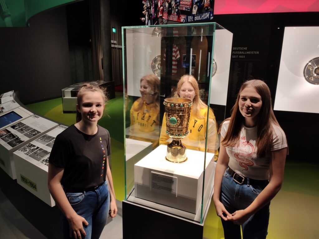 Zwei Mädchen stehen neben einer Vitrine mit einem Pokal in einem Museum.