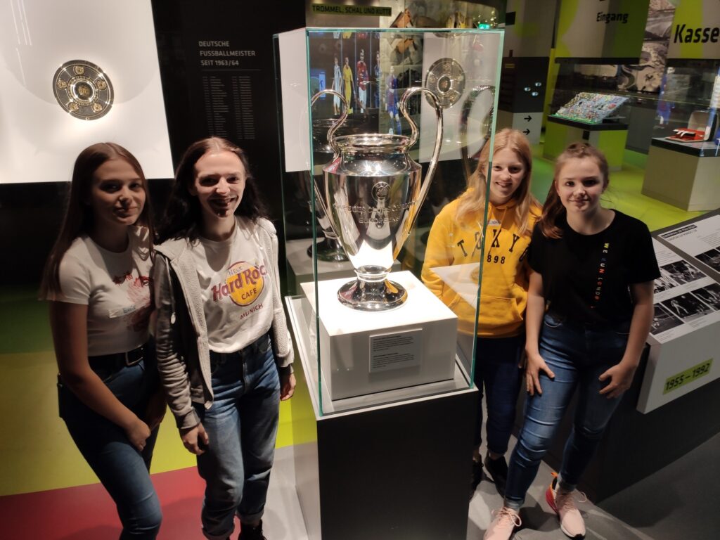 Schülerinnen posieren vor einem Pokal in einem Museum.