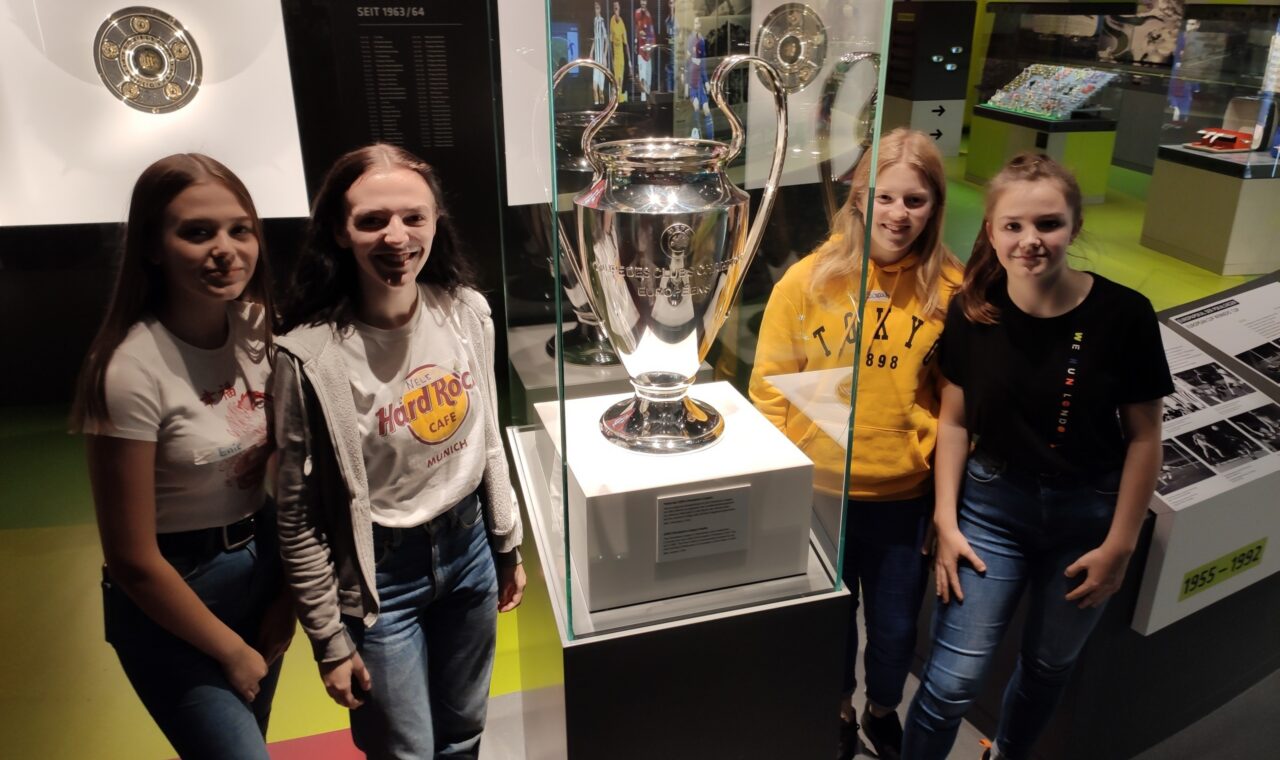 Schülerinnen posieren vor einem Pokal in einem Museum.