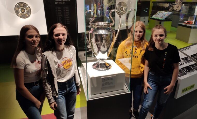 Schülerinnen posieren vor einem Pokal in einem Museum.