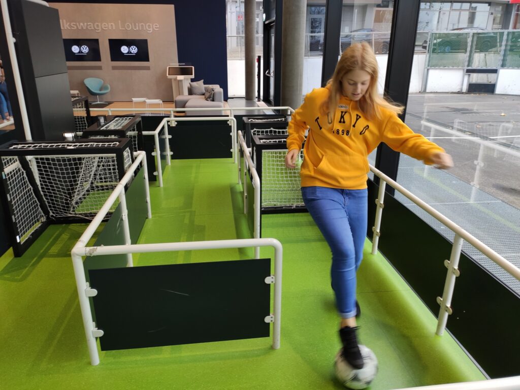 Mädchen spielt Fußball in einer Spielarena mit kleinen Toren.