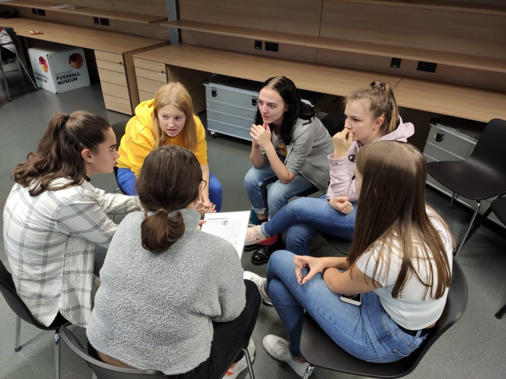 Sechs Schüler sitzen im Kreis und diskutieren konzentriert.