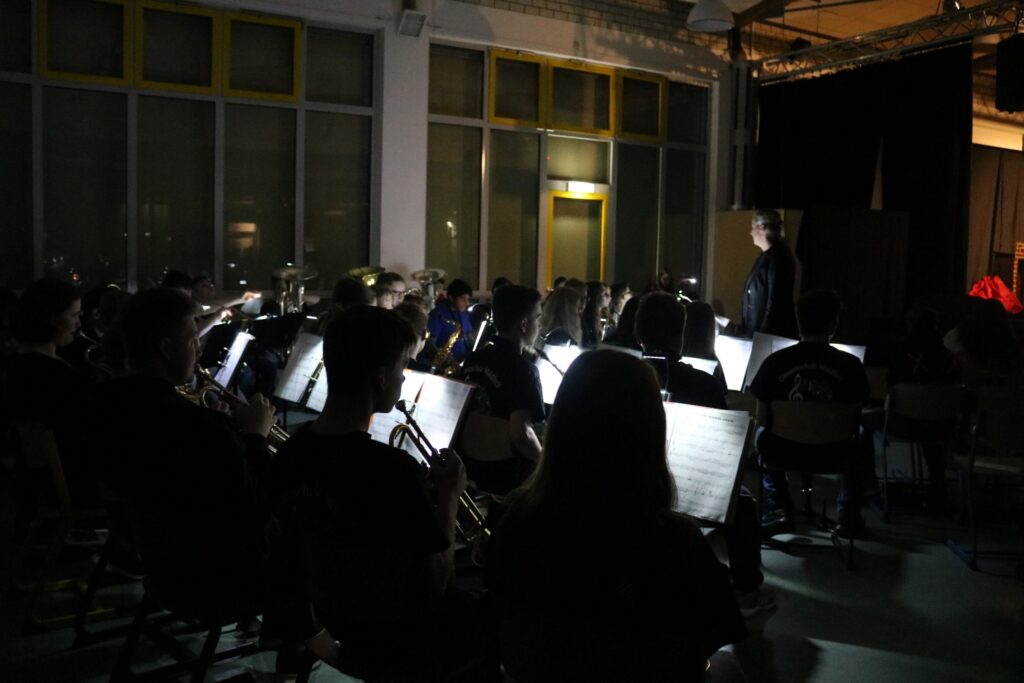 Orchesterprobe in einem dunklen Raum mit einer Gruppe von Musikern und Partituren.