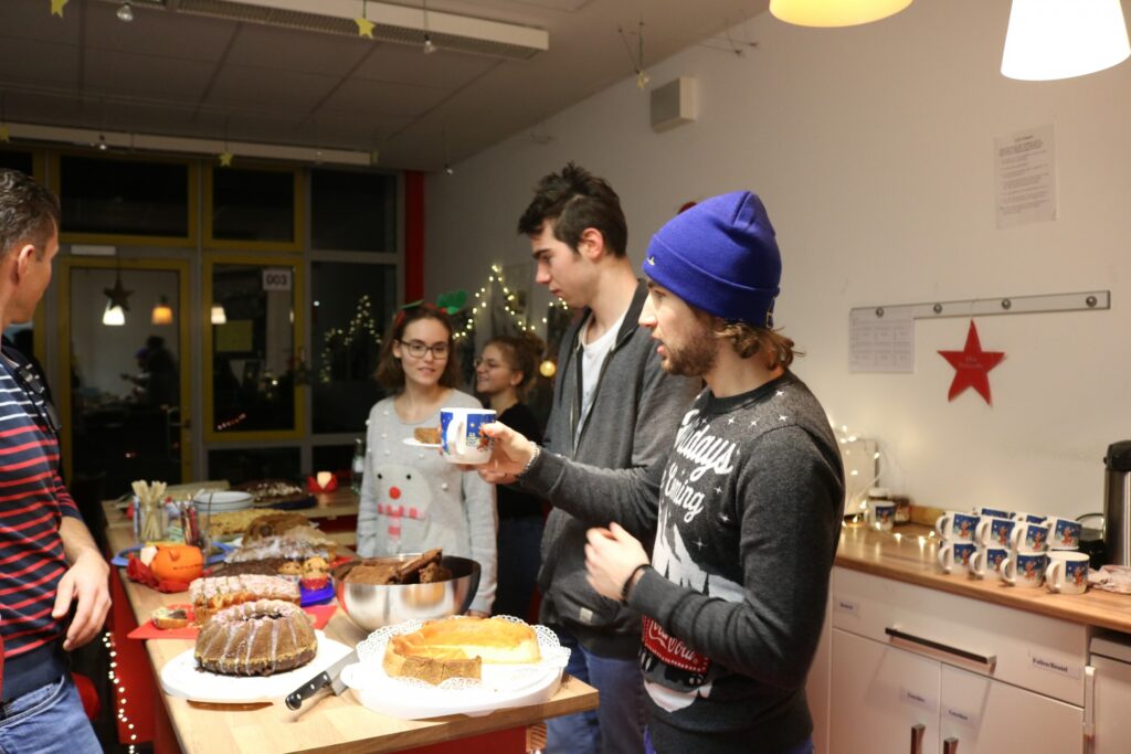 Gruppe von Jugendlichen in einer Küche mit Kuchen und Getränken bei einer Feier.