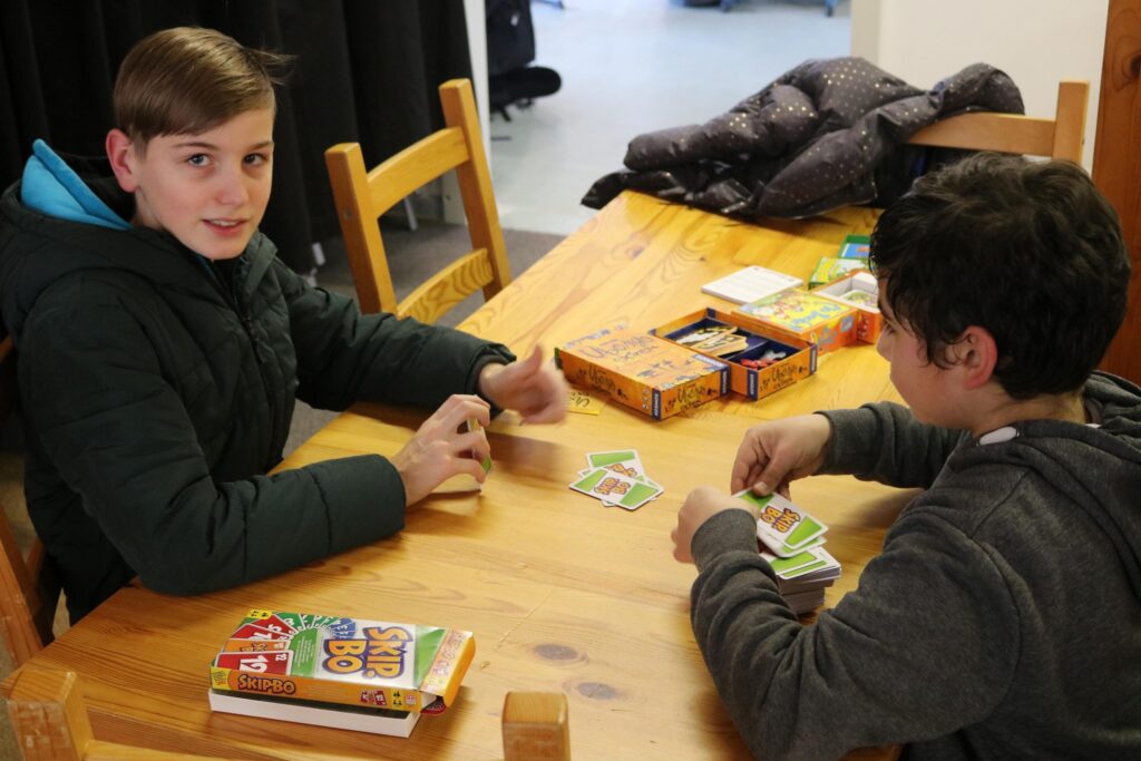 Zwei Schüler sitzen an einem Tisch und spielen ein Kartenspiel.