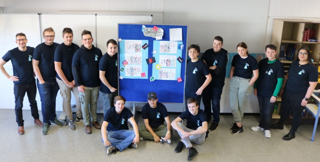 Gruppe von Schülern mit T-Shirts vor einem Plakat in einem Klassenraum.