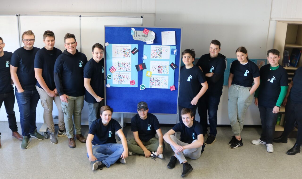 Gruppe von Schülern mit T-Shirts vor einem Plakat in einem Klassenraum.