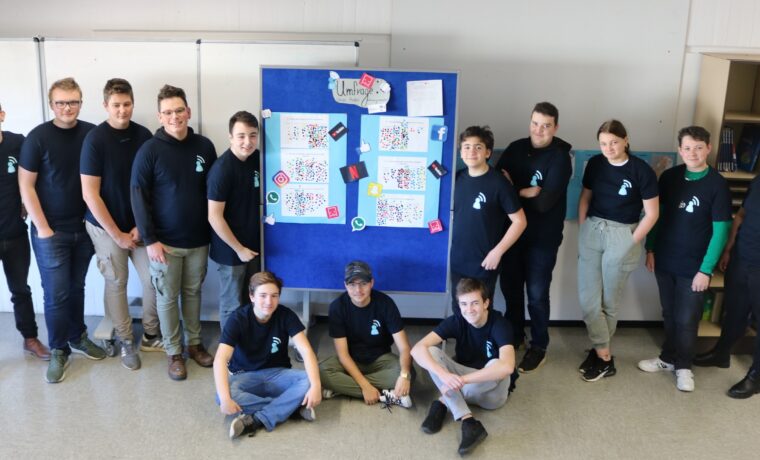 Gruppe von Schülern mit T-Shirts vor einem Plakat in einem Klassenraum.