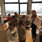 Schülerinnen und Schüler stehen in einem Klassenraum und sprechen miteinander.