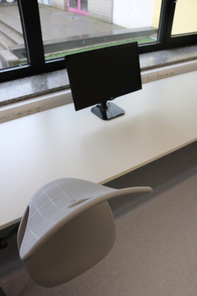 Schreibtisch mit Stuhl und Computerbildschirm in einem Klassenraum.