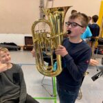 Schüler spielt Tuba, ein weiterer Schüler sitzt lächelnd daneben.