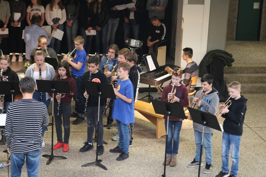 Schüler spielen Blasinstrumente in einer Aula während einer Aufführung.