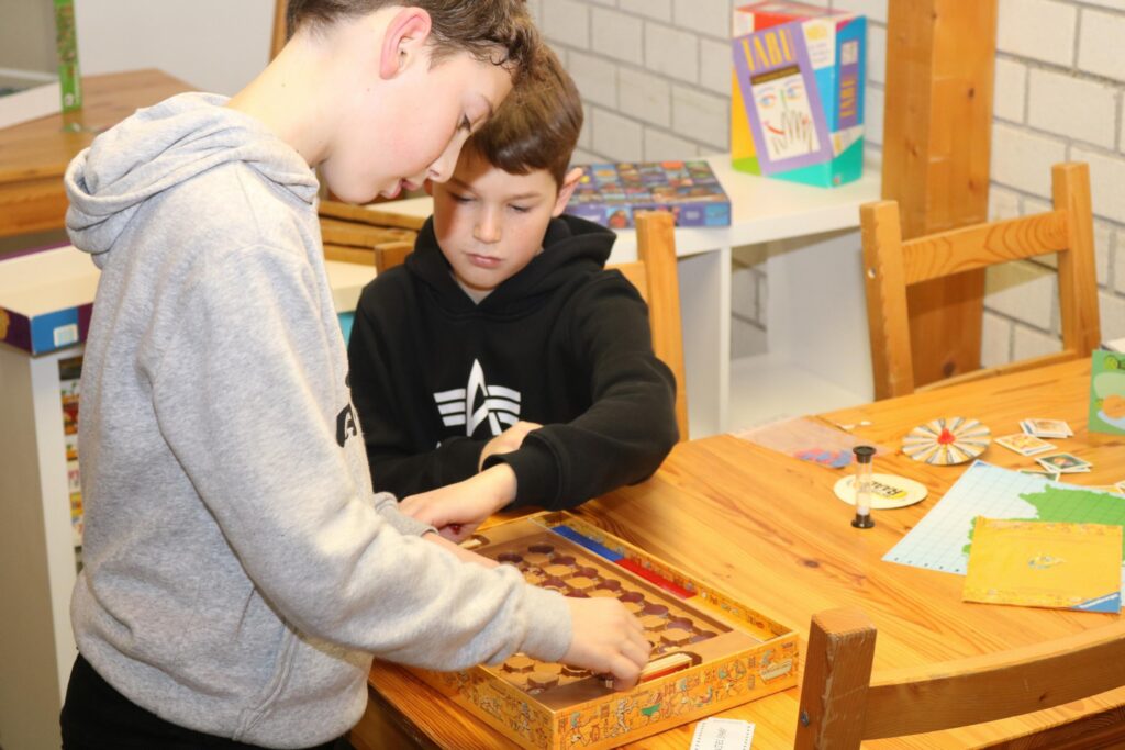 Zwei Jungen spielen ein Brettspiel an einem Tisch.