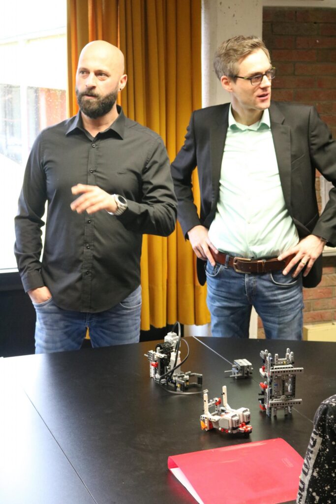 Zwei Männer stehen an einem Tisch mit Robotermodellen und diskutieren.