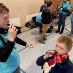 Kinder in blauen T-Shirts spielen Musikinstrumente in einer Turnhalle.