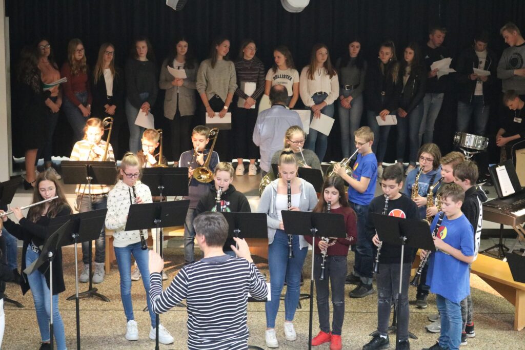 Schulband und Chor bei einer Aufführung in der Aula, zahlreiche Schüler beteiligt.