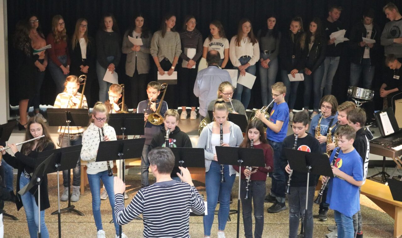 Schulband und Chor bei einer Aufführung in der Aula, zahlreiche Schüler beteiligt.