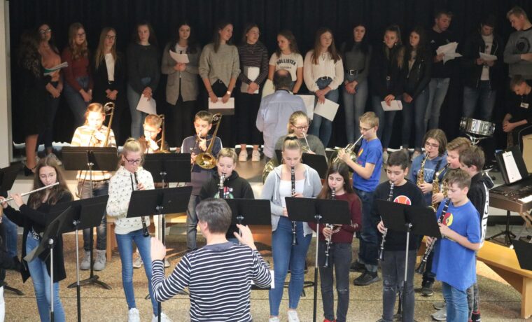 Schulband und Chor bei einer Aufführung in der Aula, zahlreiche Schüler beteiligt.