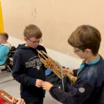 Zwei Kinder stehen in einer Halle und zeigen sich gegenseitig ein Instrument.
