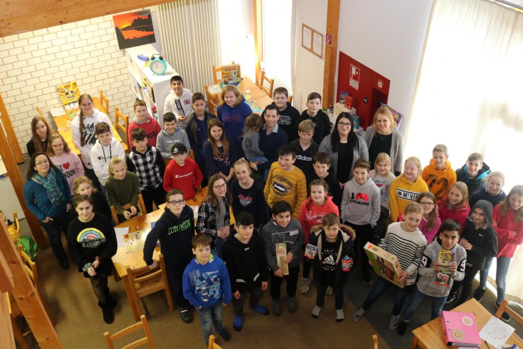 Gruppe von Schülern steht lächelnd in einem Klassenraum.