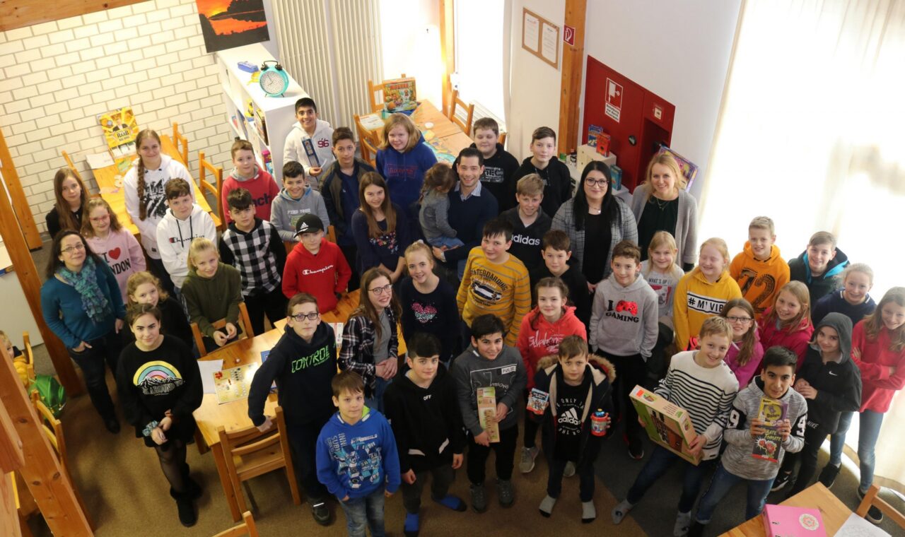 Gruppe von Schülern steht lächelnd in einem Klassenraum.