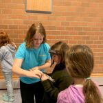 Kinder in blauen T-Shirts arbeiten zusammen an einem Projekt in einer Turnhalle.